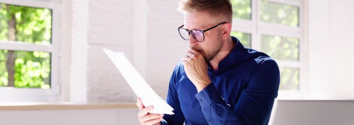 man in blue shirt with glasses looking at pieces of paper