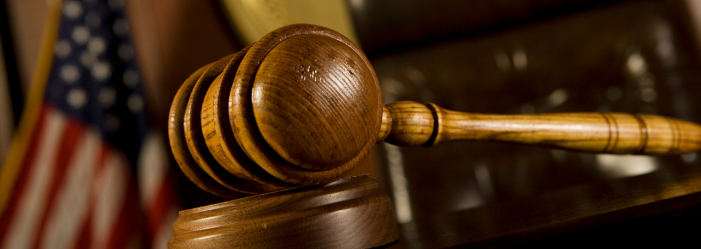 wooden gavel with a flag behind it representing court