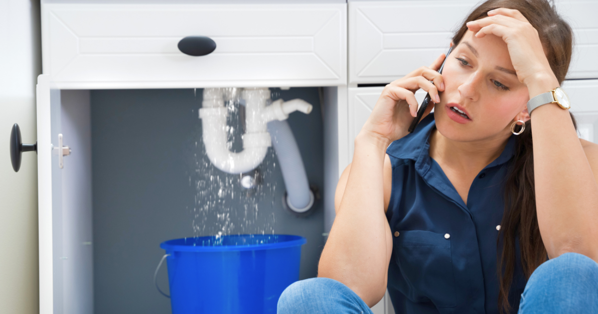 woman on the phone with her hand on her head, leaking pipe behind her with bucket underneath representing a landlord not making repairs