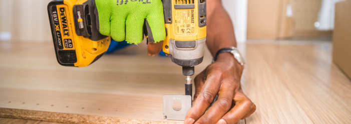 person with green gloves on, drilling something into wood