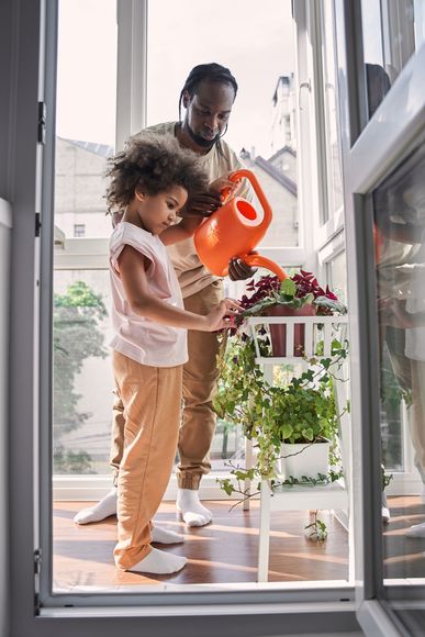 A man and a little girl are watering plants on a balcony.