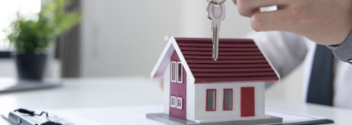 Small model house with a person handing over a set of keys, symbolizing landlord-tenant housing righ