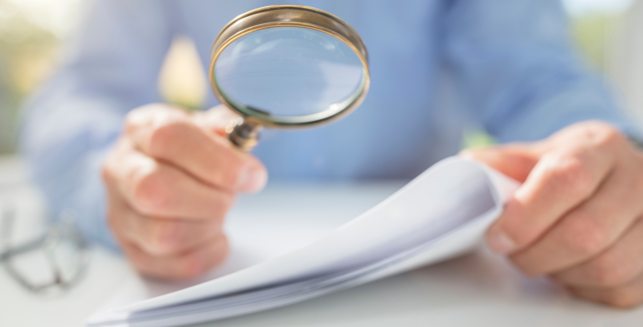 Person holding a stack of papers, holding a magnifying glass up to the papers