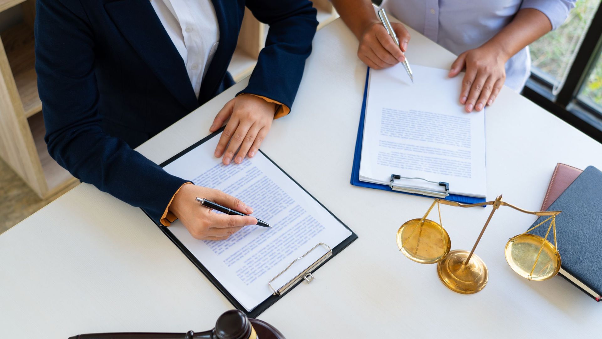 two people sitting with paperwork on clipboards, there is a gold scale representing legal support