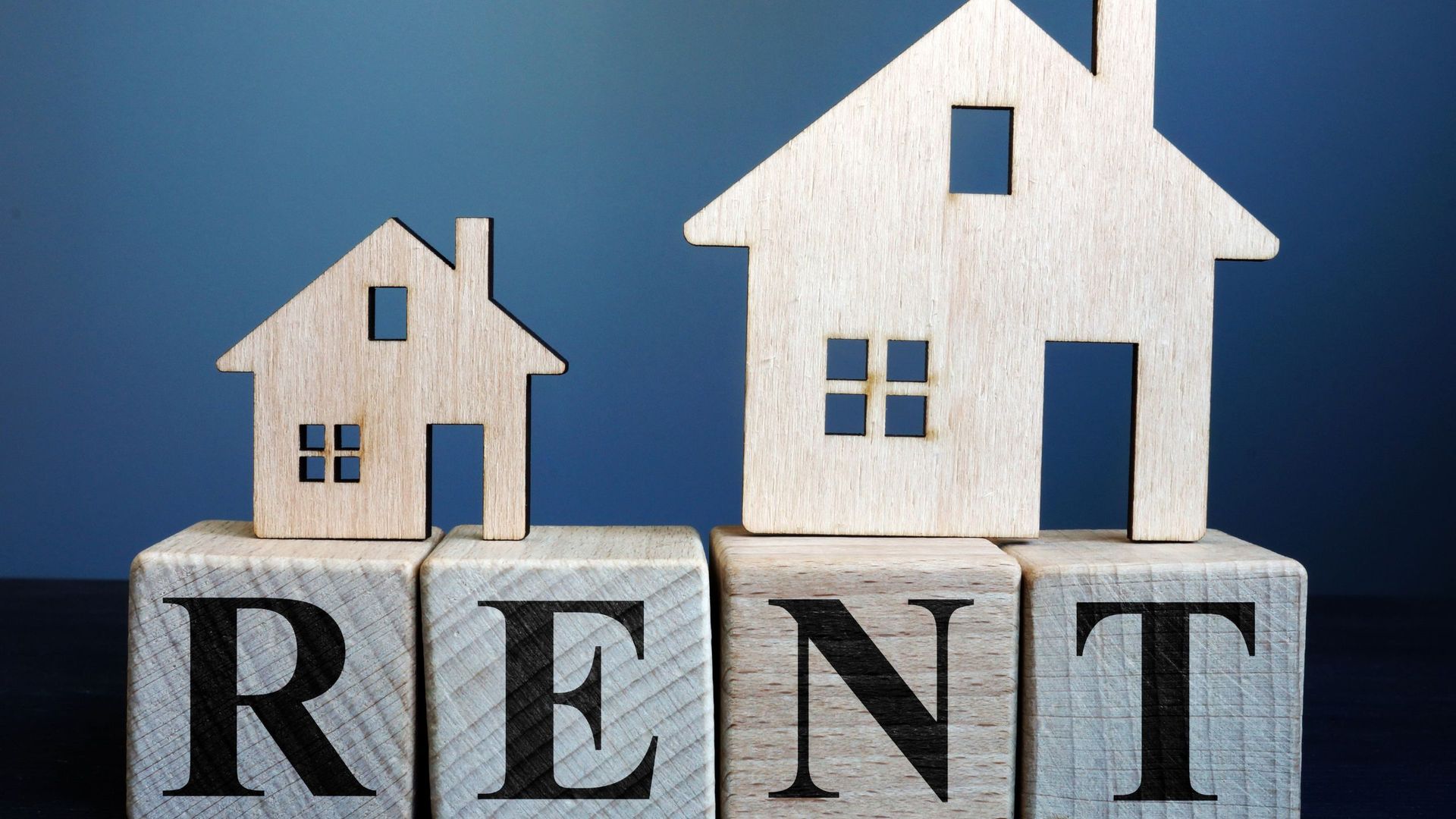 Wooden blocks that spell out RENT with two wooden houses on top