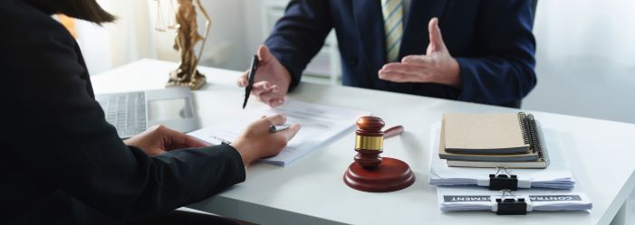 two attorneys sitting across from each other with their hands open holding pens, there's a gavel and a statue of justice in the background