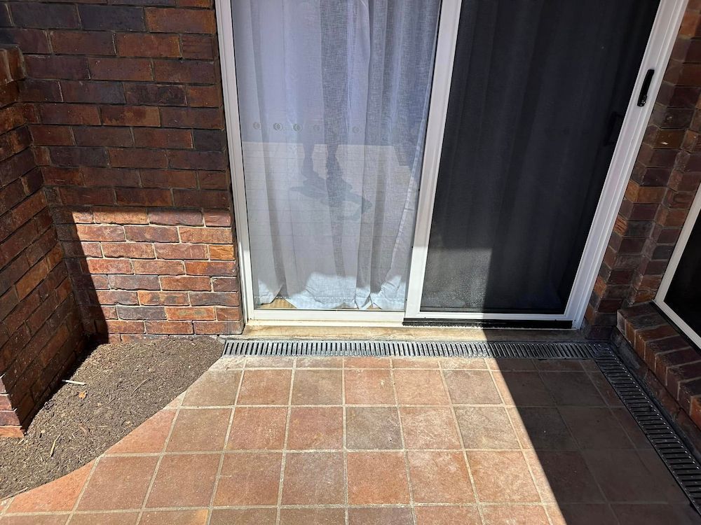 A Brick Building With a Sliding Glass Door and a Tiled Floor — Otto’s Plumbing & Gasfitting in Arana Hills, QLD