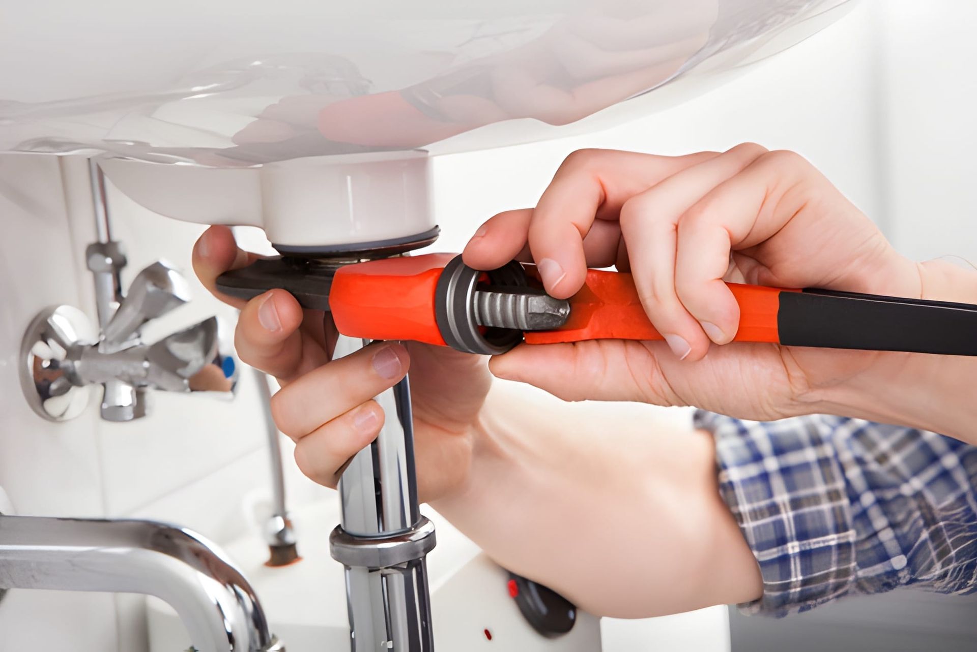 Plumber Using a Wrench to Work on the Plumbing Under a White Sink — Otto’s Plumbing & Gasfitting in Wavell Heights, QLD