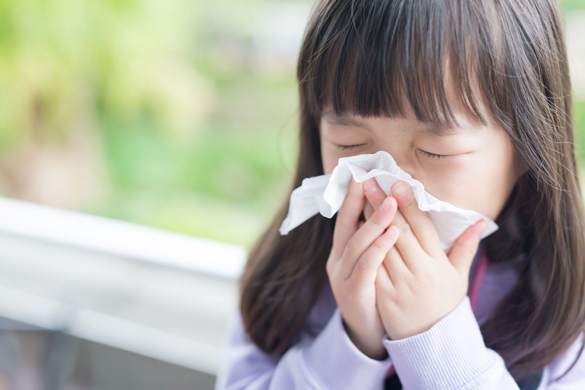 A young girl blowing her nose due to allergy.