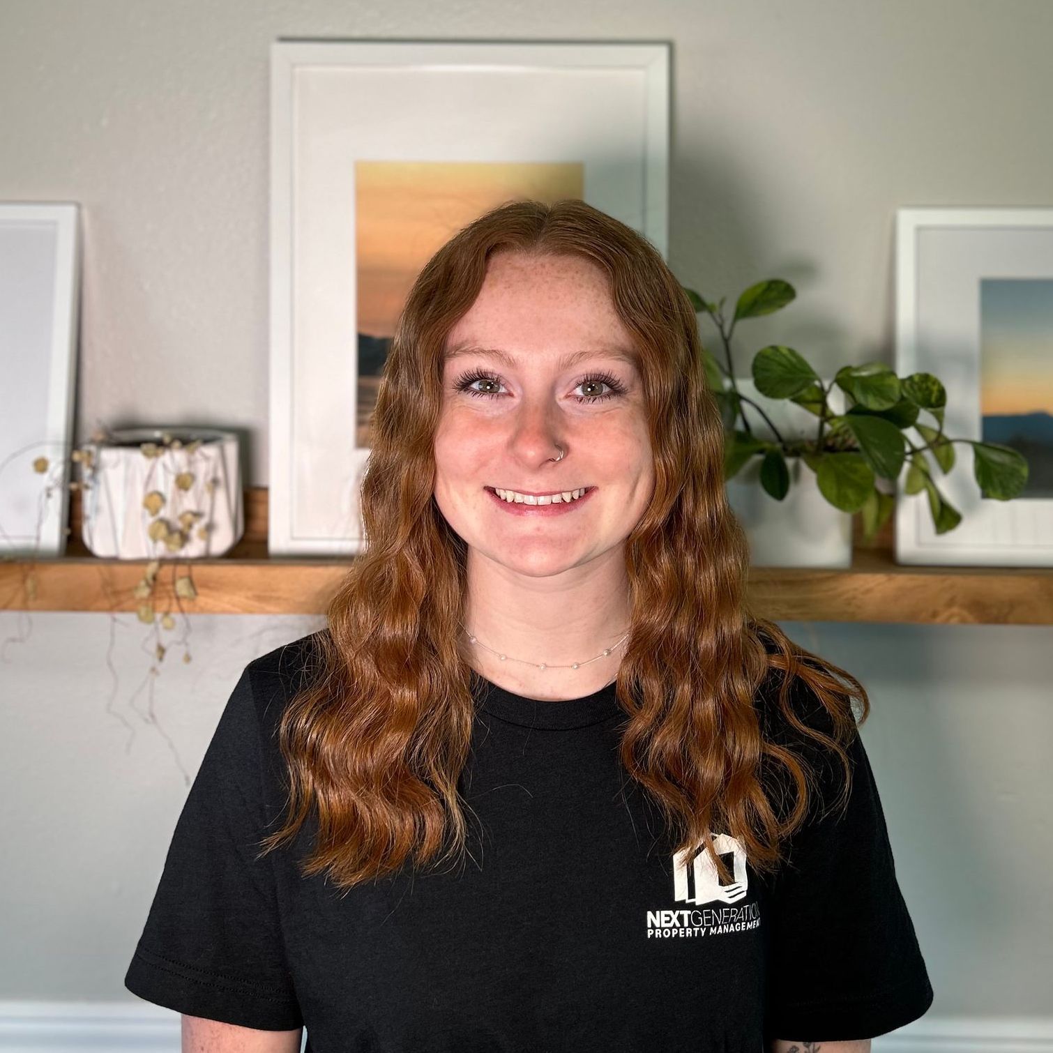 A woman with long red hair is wearing a black shirt and smiling.