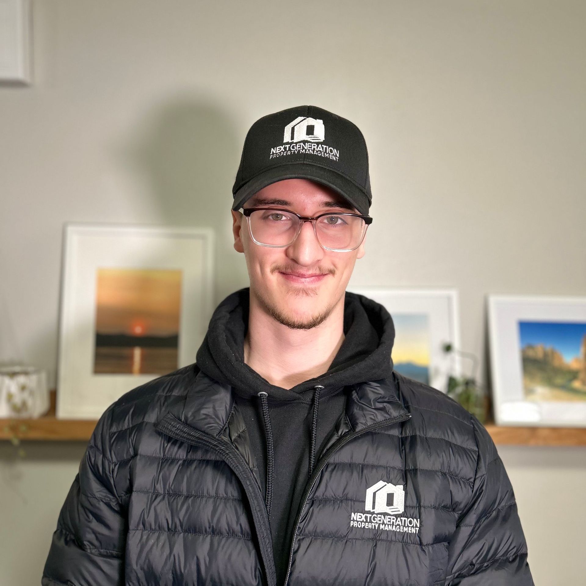 A man wearing a hat and glasses is standing in front of a wall.