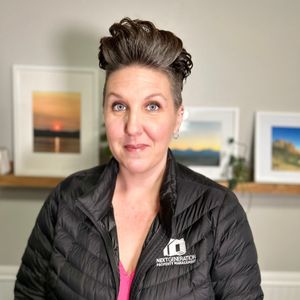 A woman wearing a black jacket is standing in front of a shelf with pictures on it.