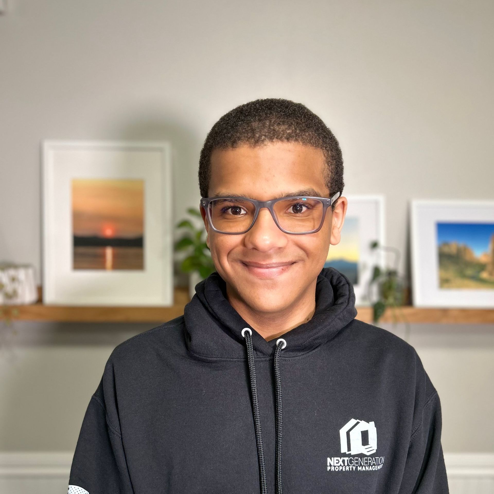 A young boy wearing glasses and a black hoodie is smiling for the camera.
