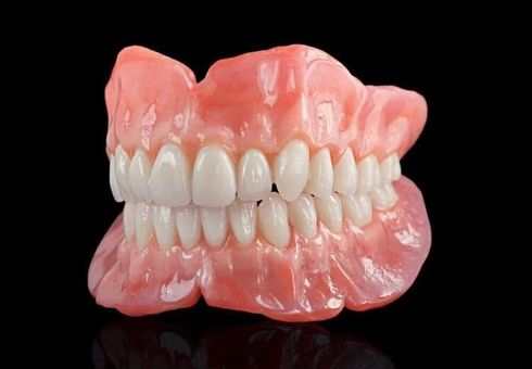 Set of complete dentures with pink gums and white teeth, against a black background.