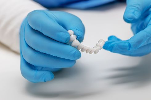 Hands in blue gloves hold a dental appliance with white teeth.