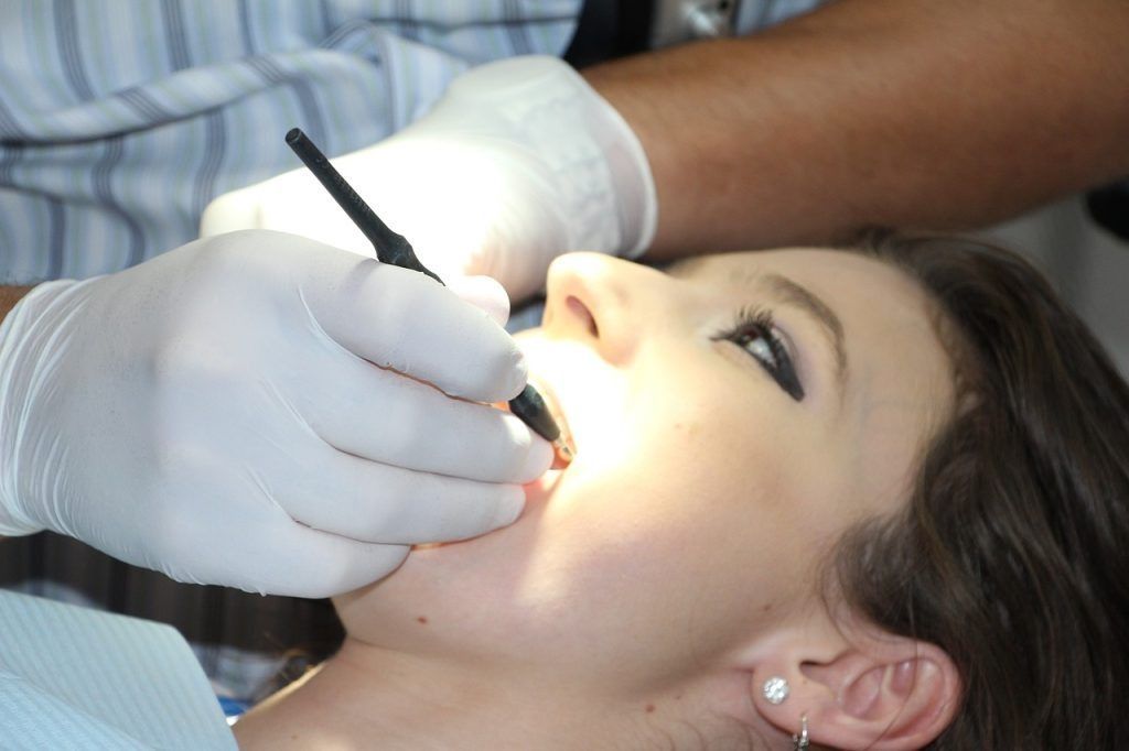 Dentist examining woman's teeth with a dental tool in a dental office.