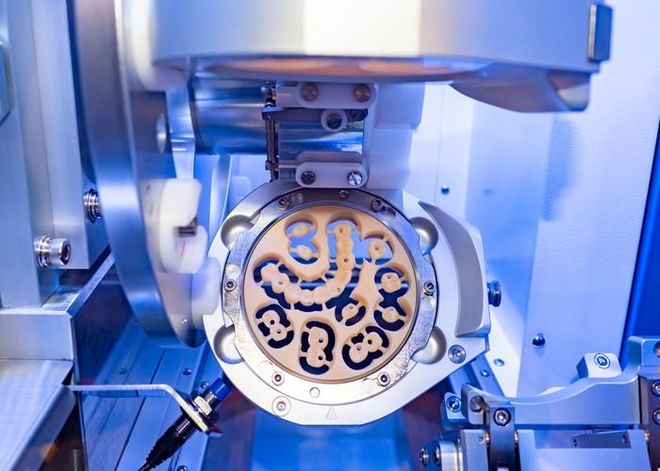 A dental milling machine precisely carving a tooth-shaped restoration from a beige block.