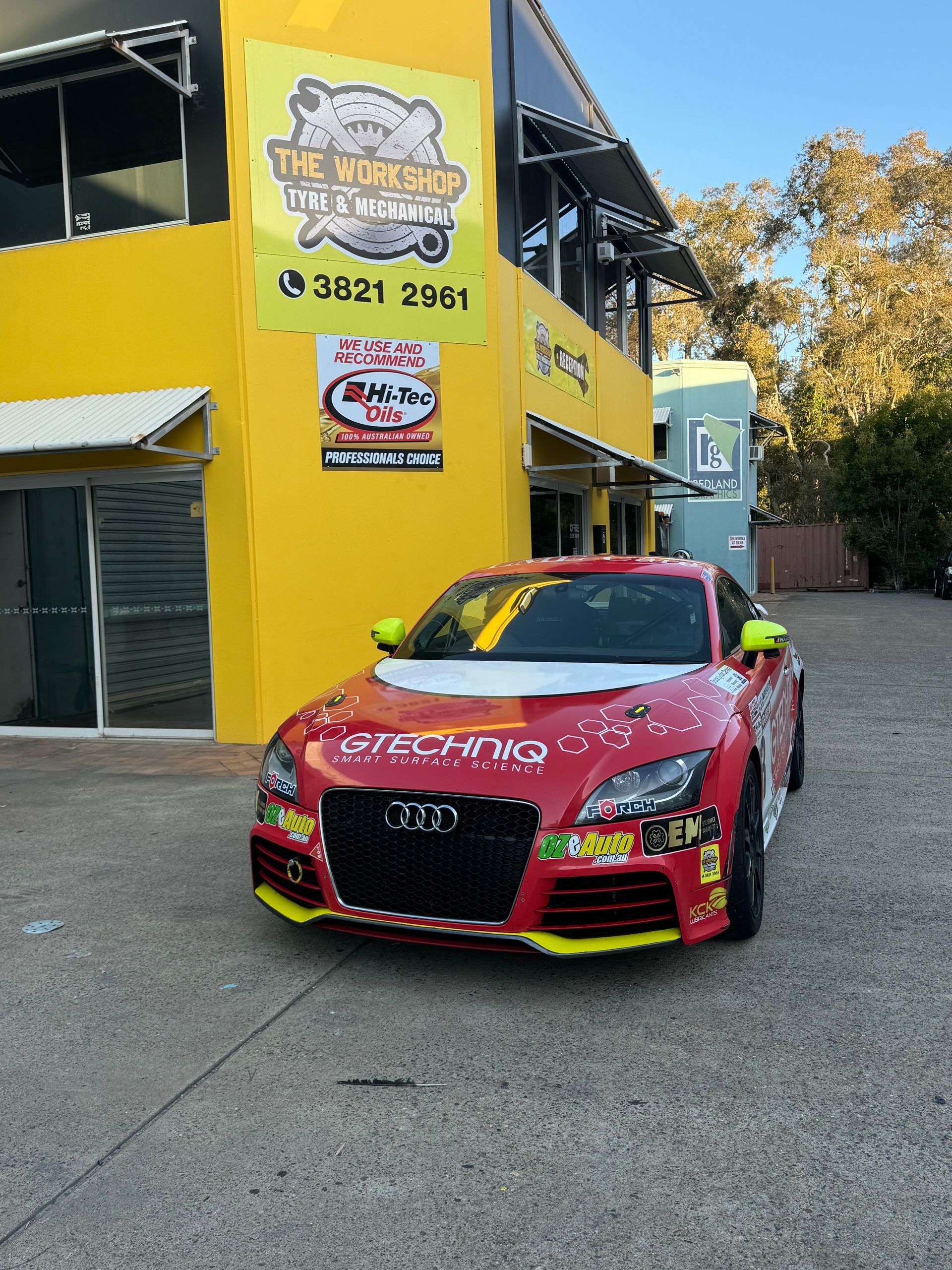 A red car is parked in front of a yellow building. — HO Performance in Cleveland, QLD