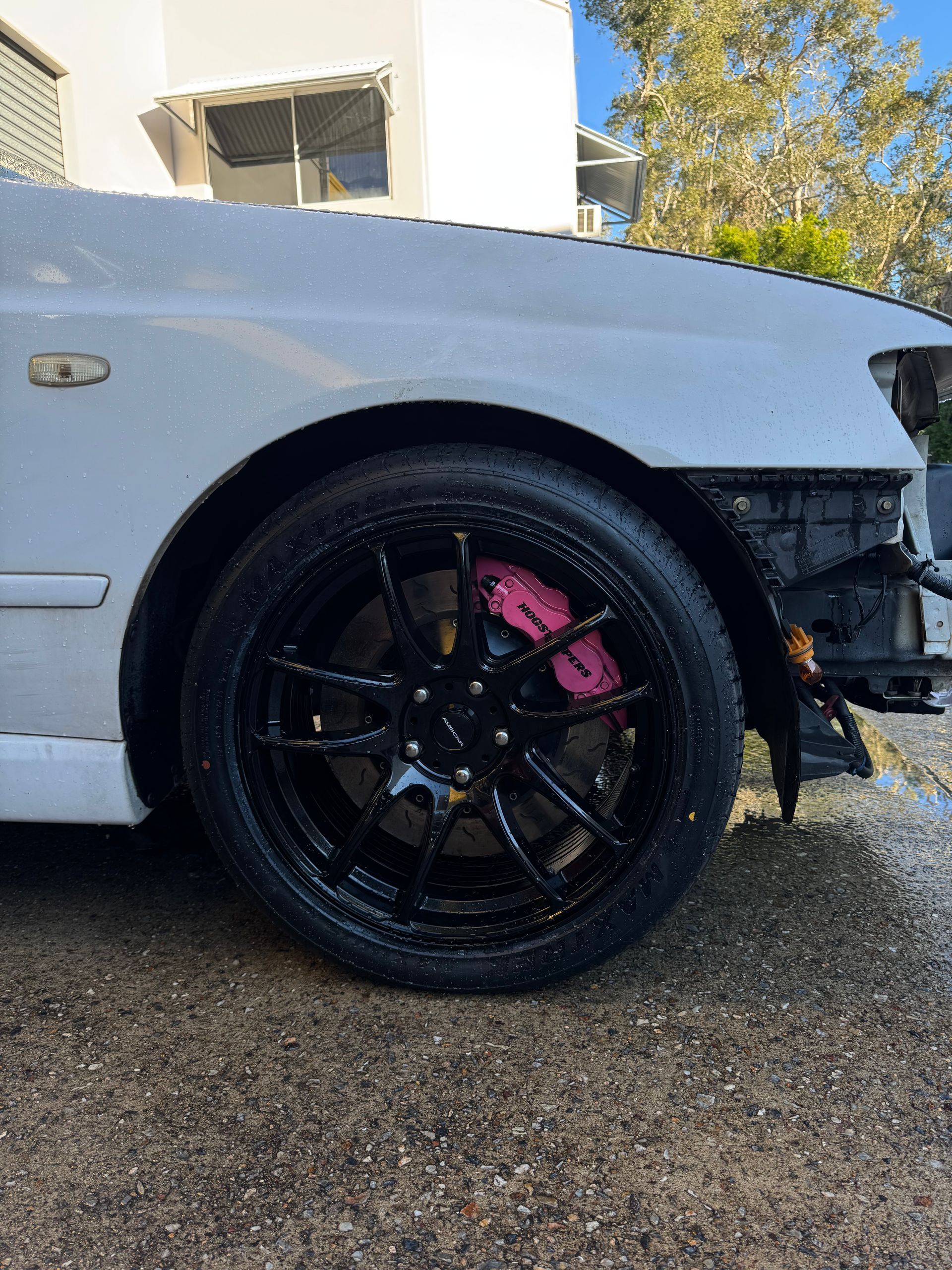 A white car with black wheels and pink brake calipers is parked on the side of the road. — HO Performance in Cleveland, QLD