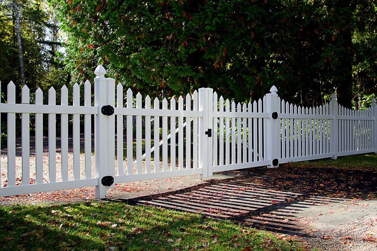 a white picket fence surrounds a driveway with trees in the background .