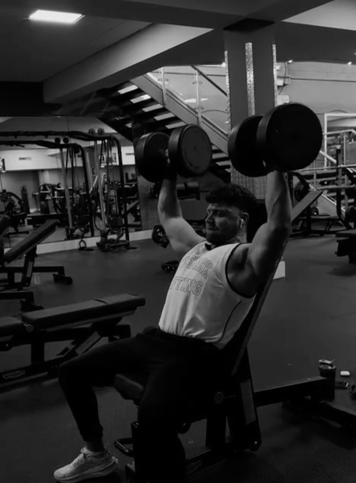 A man is lifting dumbbells in a gym in a black and white photo.