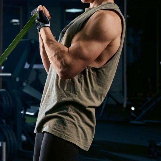 A man in a tank top is holding a green resistance band