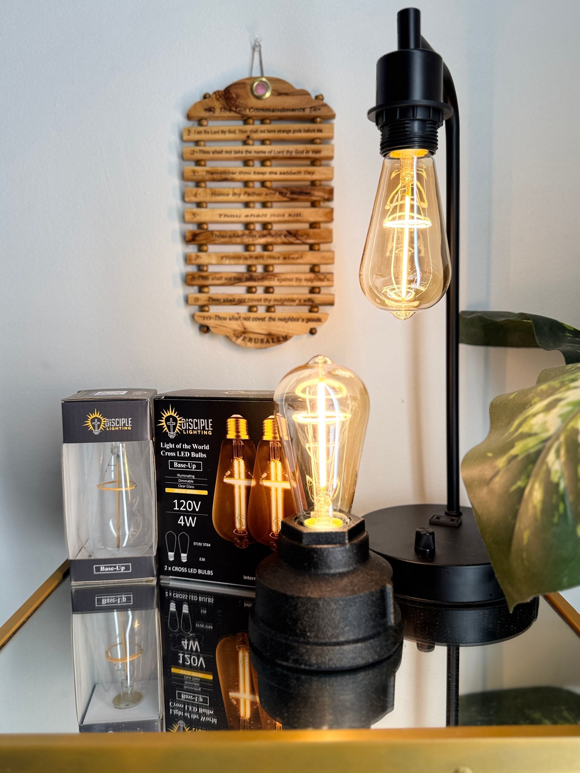 Black desk lamp with Edison bulb and another lit Edison bulb on a small base; a bamboo pot holder hangs on the wall.