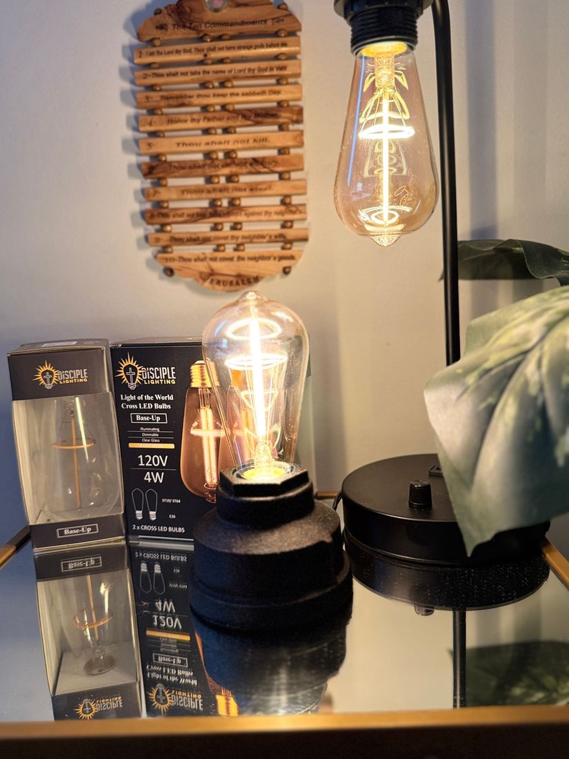 Black desk lamp with Edison bulb; the bulb is lit. A wood wall hanging and the lamp's box are visible too.