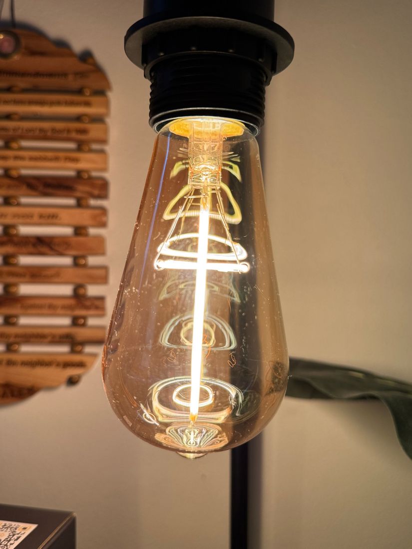 Close-up of a lit Edison-style light bulb with a visible filament, against a blurred background.