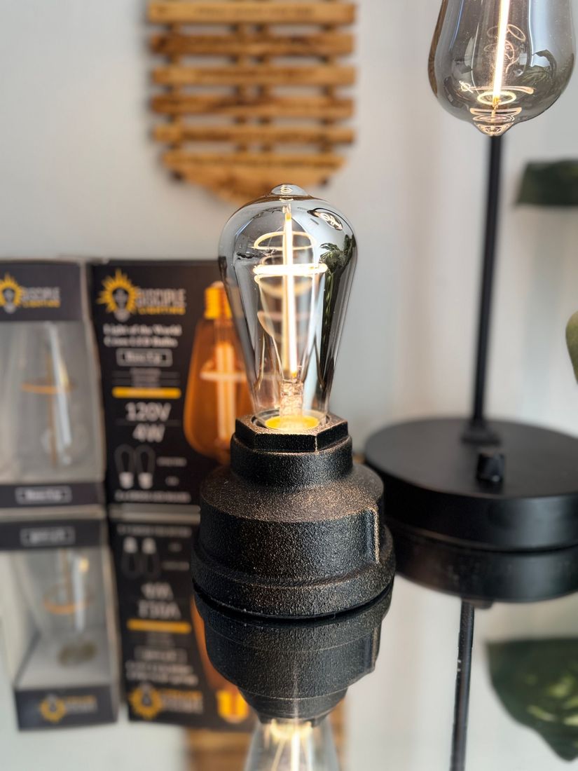 Close-up of a vintage-style light bulb in a black base, with a box and other lights in the background.
