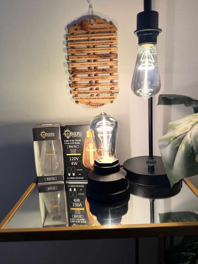 A mirrored table with a lamp, a wooden pendant, and light bulbs. The black lamp has a glowing bulb.
