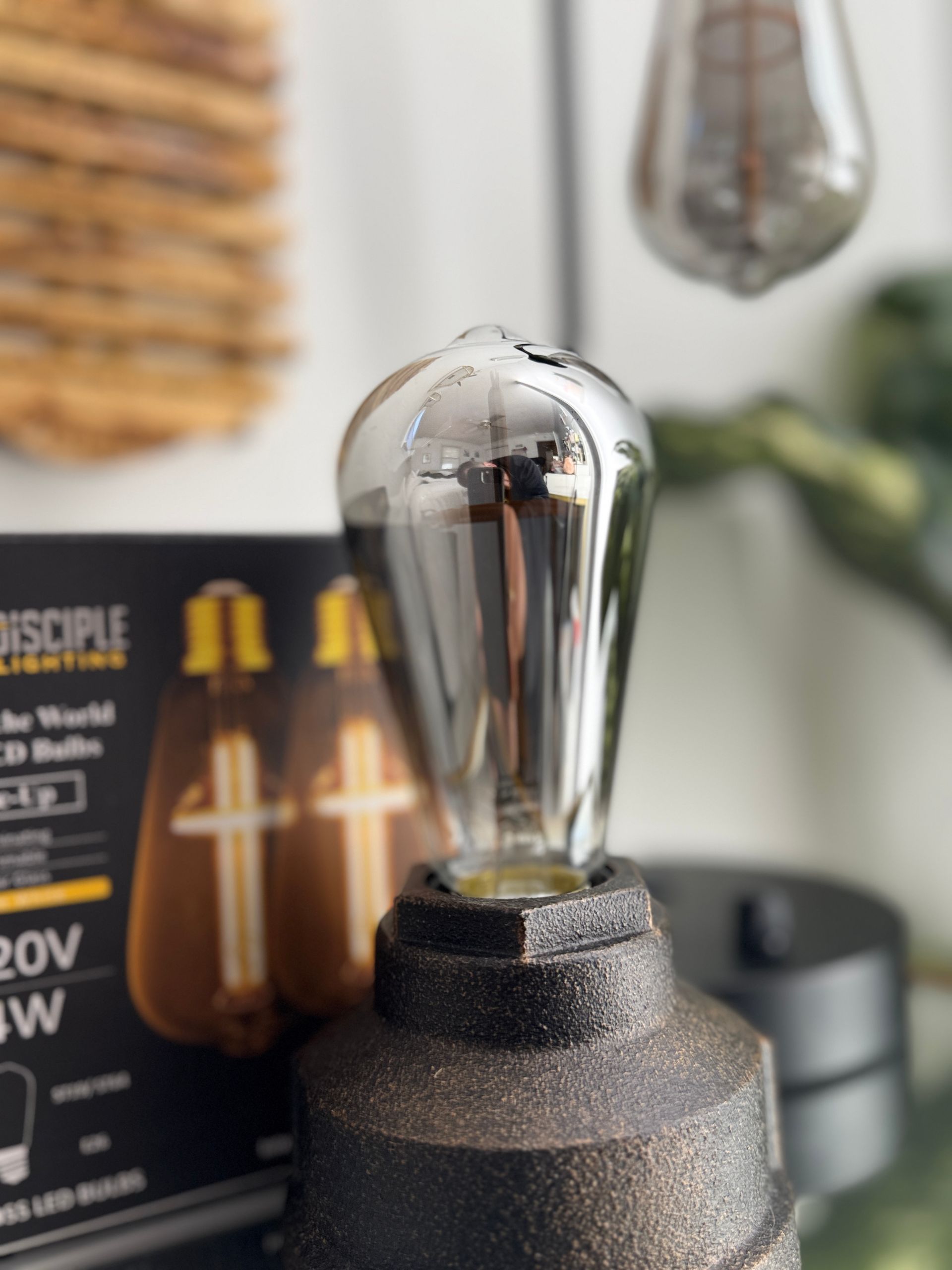 Close-up of a silver-topped lightbulb in a speckled holder, with a box of similar bulbs in the background.