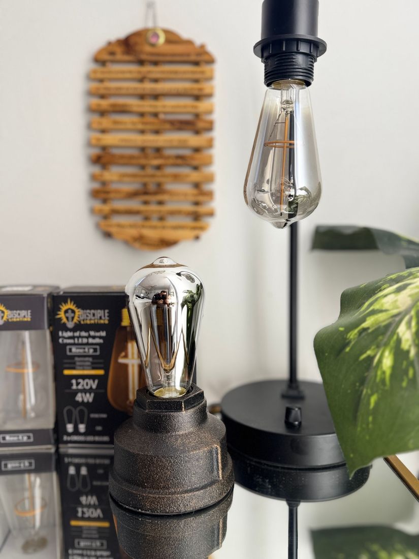 Close-up of a decorative lamp with a lit, vintage-style bulb, on a mirrored surface. 
