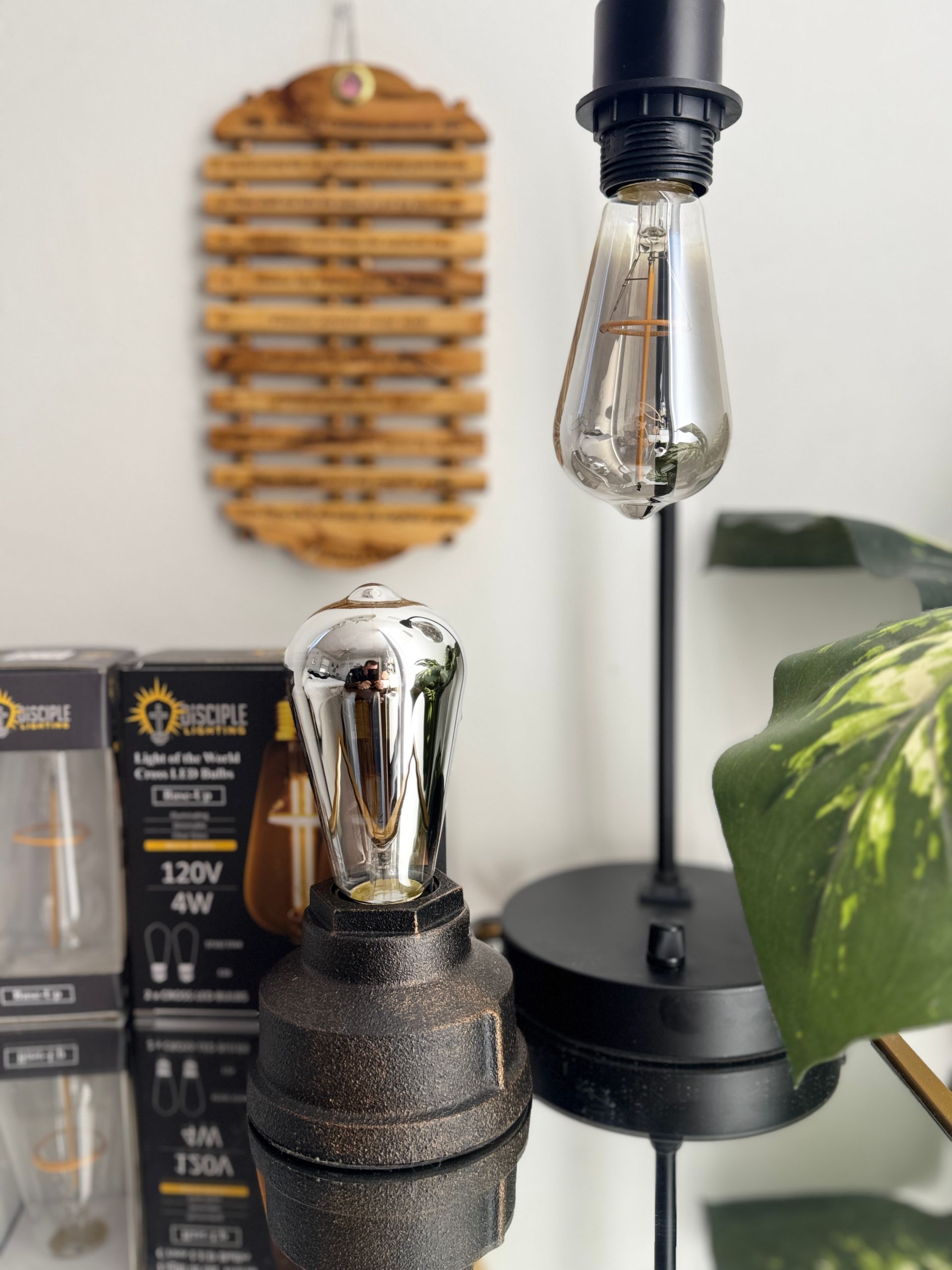 Black lamp with Edison bulb, metal lamp base, box, and decorative cross bulb on reflective surface.