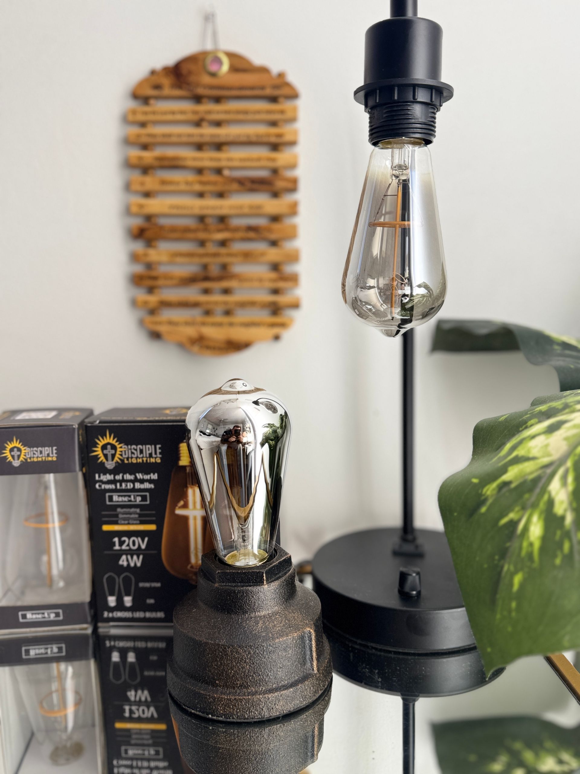 Black lamp with exposed bulb, decorative object and a plant on a reflective surface.