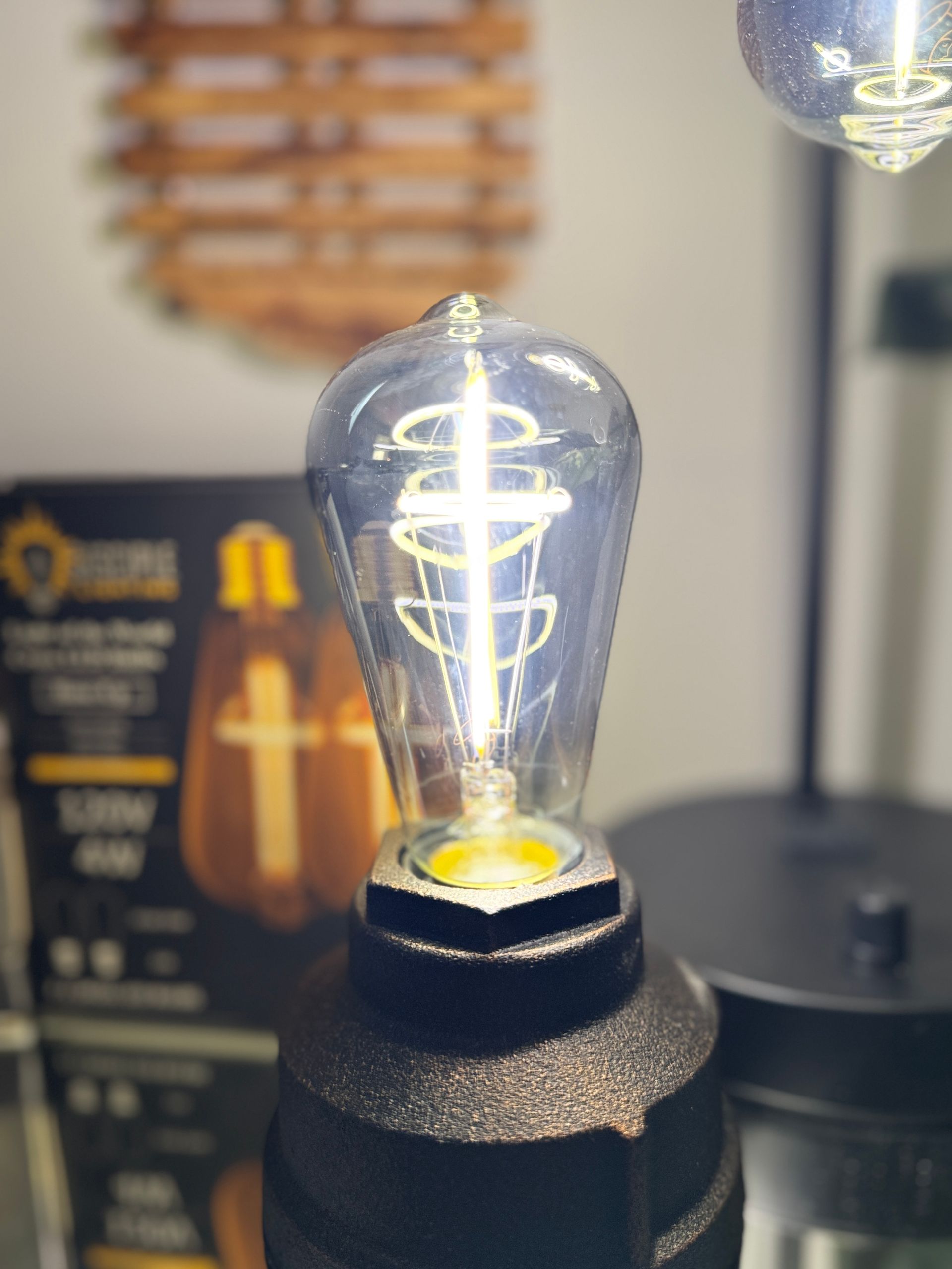 Vintage-style LED lightbulb with a decorative, swirling filament; black base, box in the background.
