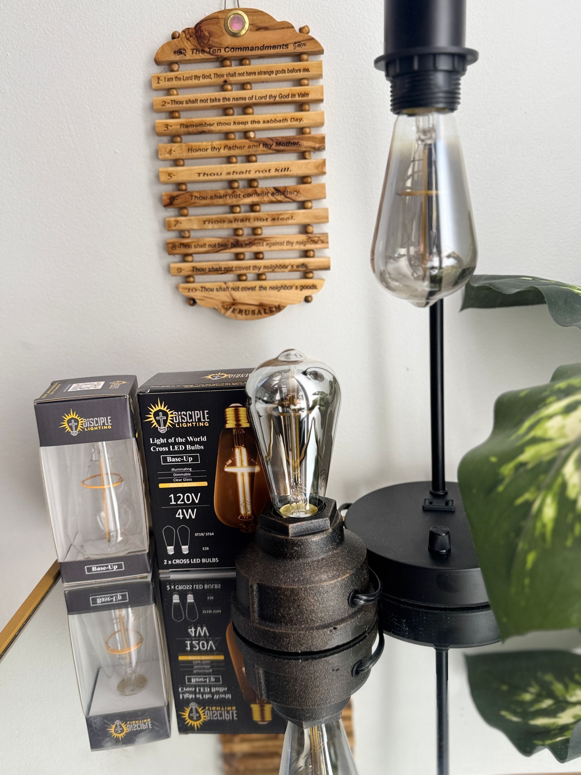 A lamp with a vintage-style bulb sits next to a wooden wall hanging and two boxes of bulbs on a mirrored surface.