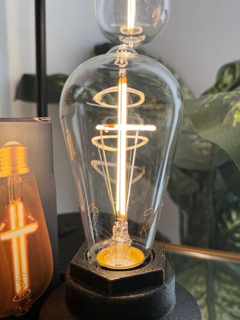 Close-up of lit, decorative Edison bulb with swirling filament. Black base, clear glass, warm light.