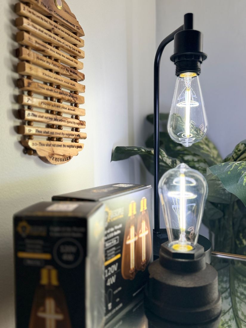 Black industrial desk lamp with Edison bulbs next to a box of bulbs and a wooden plaque on a wall.