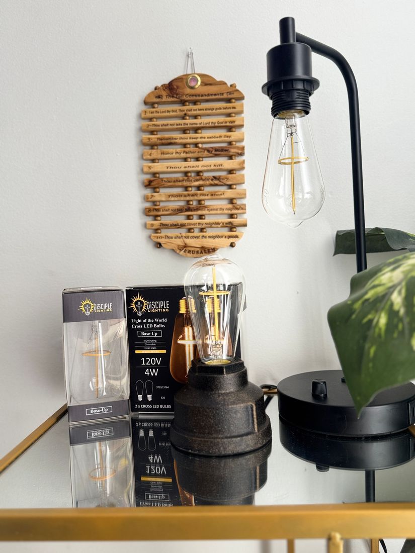 Black desk lamp with a decorative bulb, next to a bamboo wall hanging and a box of similar bulbs.