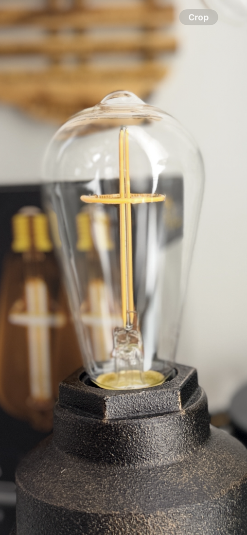 Close-up of a decorative lightbulb in a black base; the bulb features a golden cross filament.