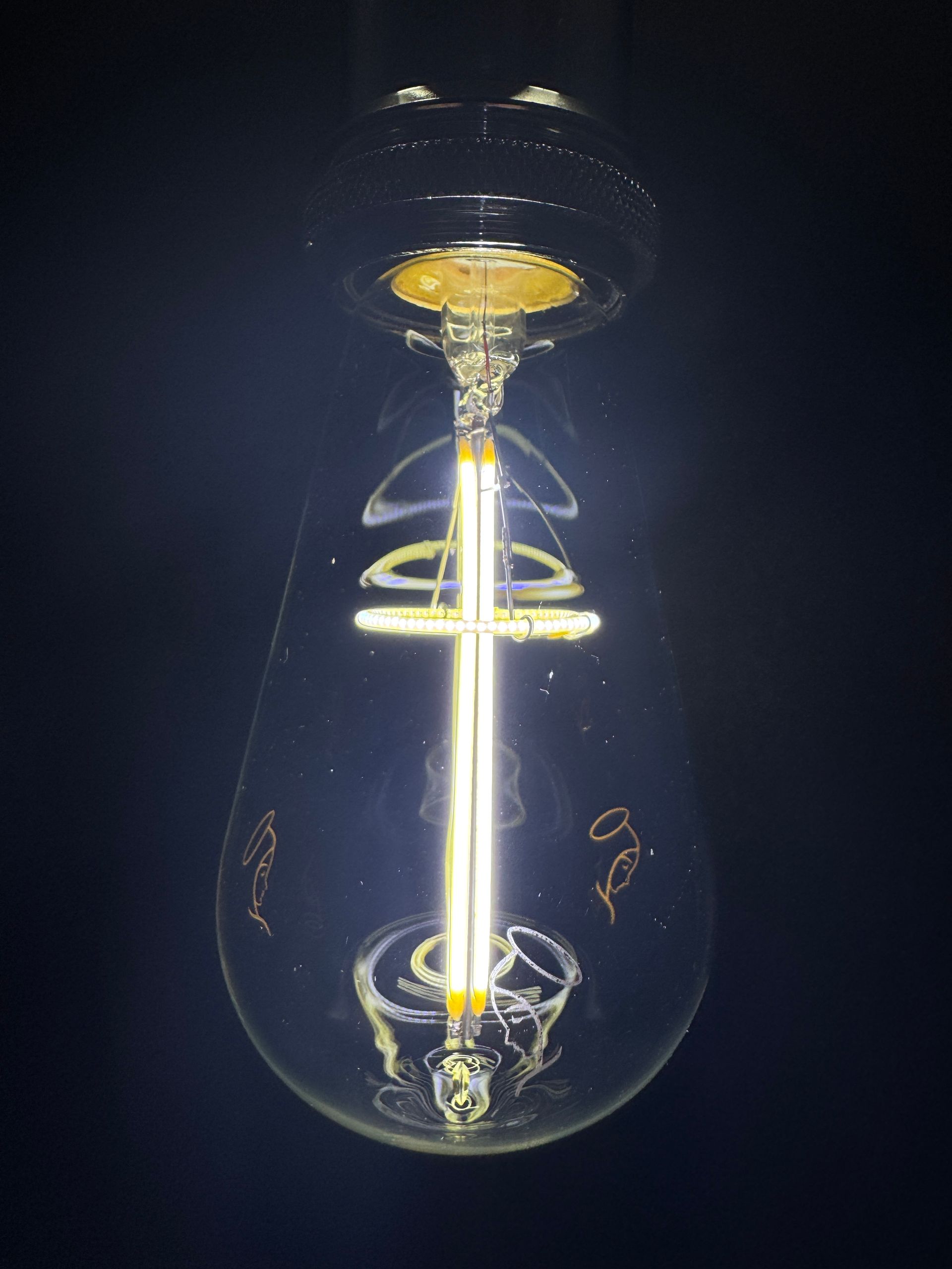 Lit Edison-style lightbulb on dark background; filament visible inside the clear glass.