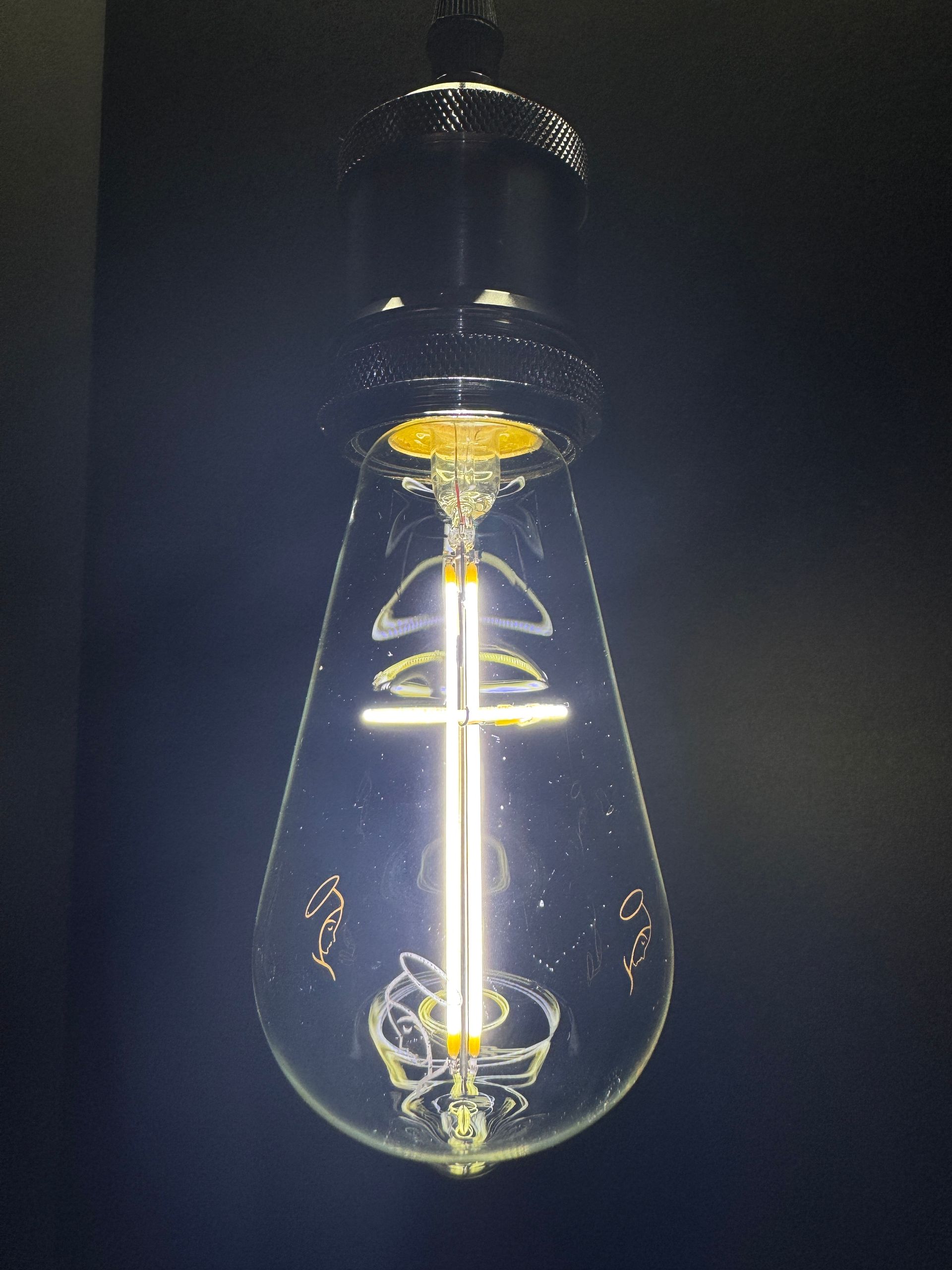 Lit teardrop-shaped light bulb, filament glowing, against a dark background.