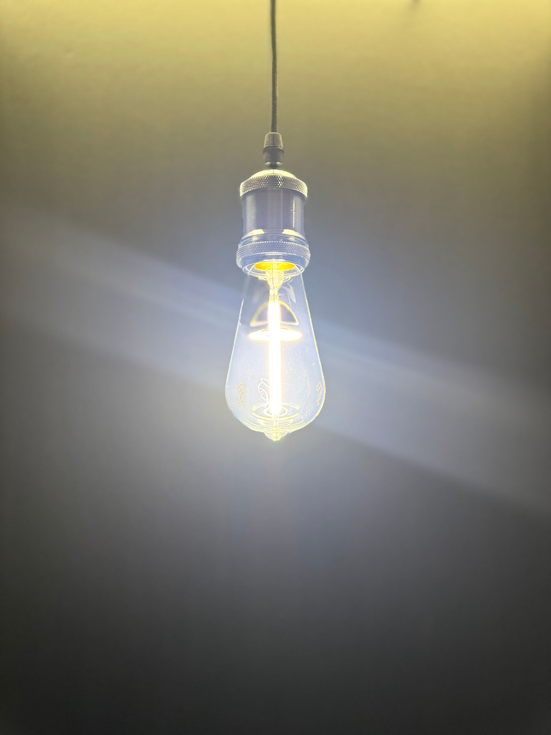 Lit Edison bulb hanging from a cord against a dim wall.