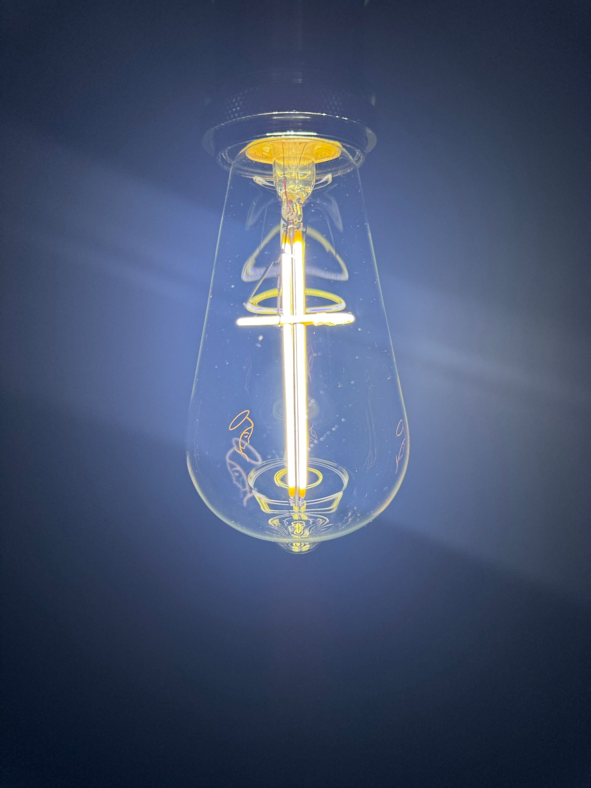 Teardrop-shaped Edison bulb illuminated against a dark blue background.