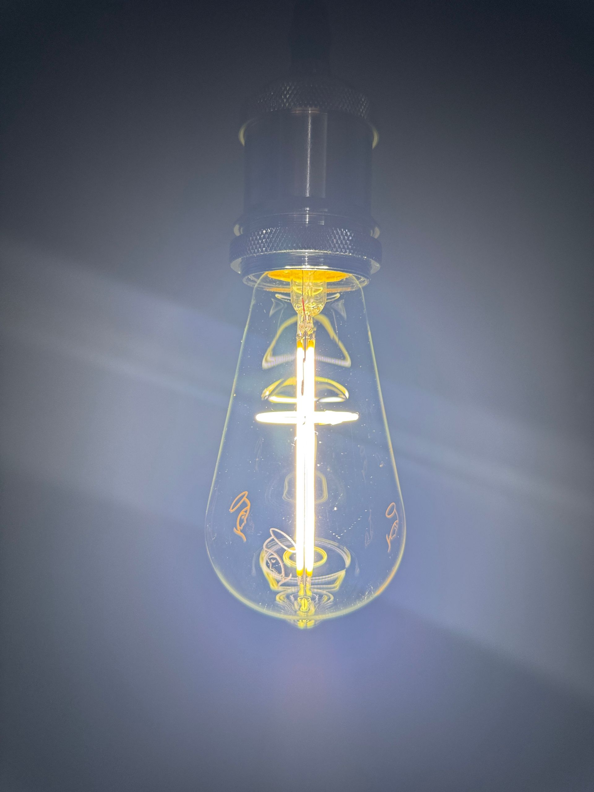 Lit, teardrop-shaped Edison bulb hangs from the ceiling. A warm yellow glow illuminates the glass.