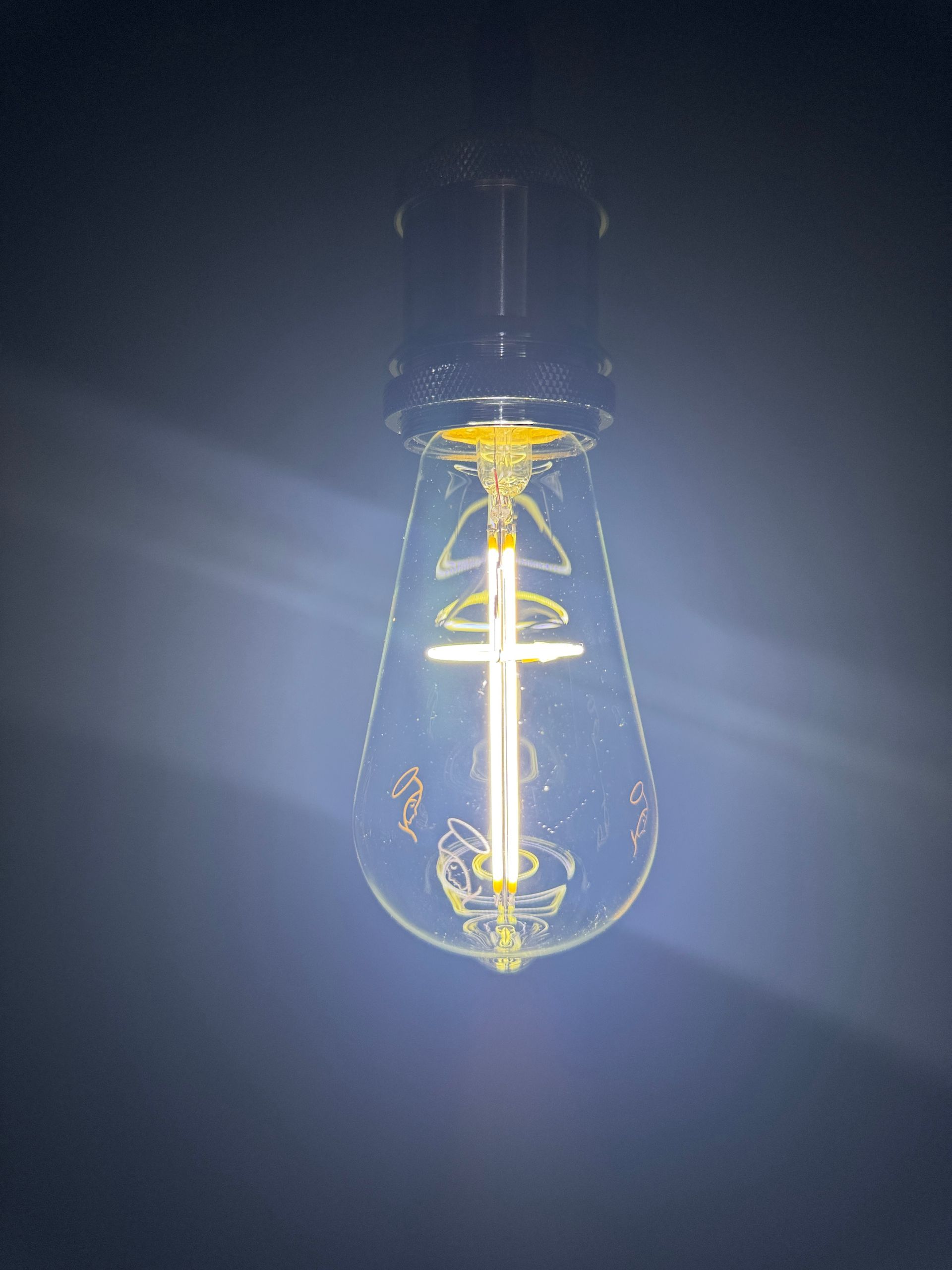 Lit Edison bulb hanging against a dark background, glowing with warm light.