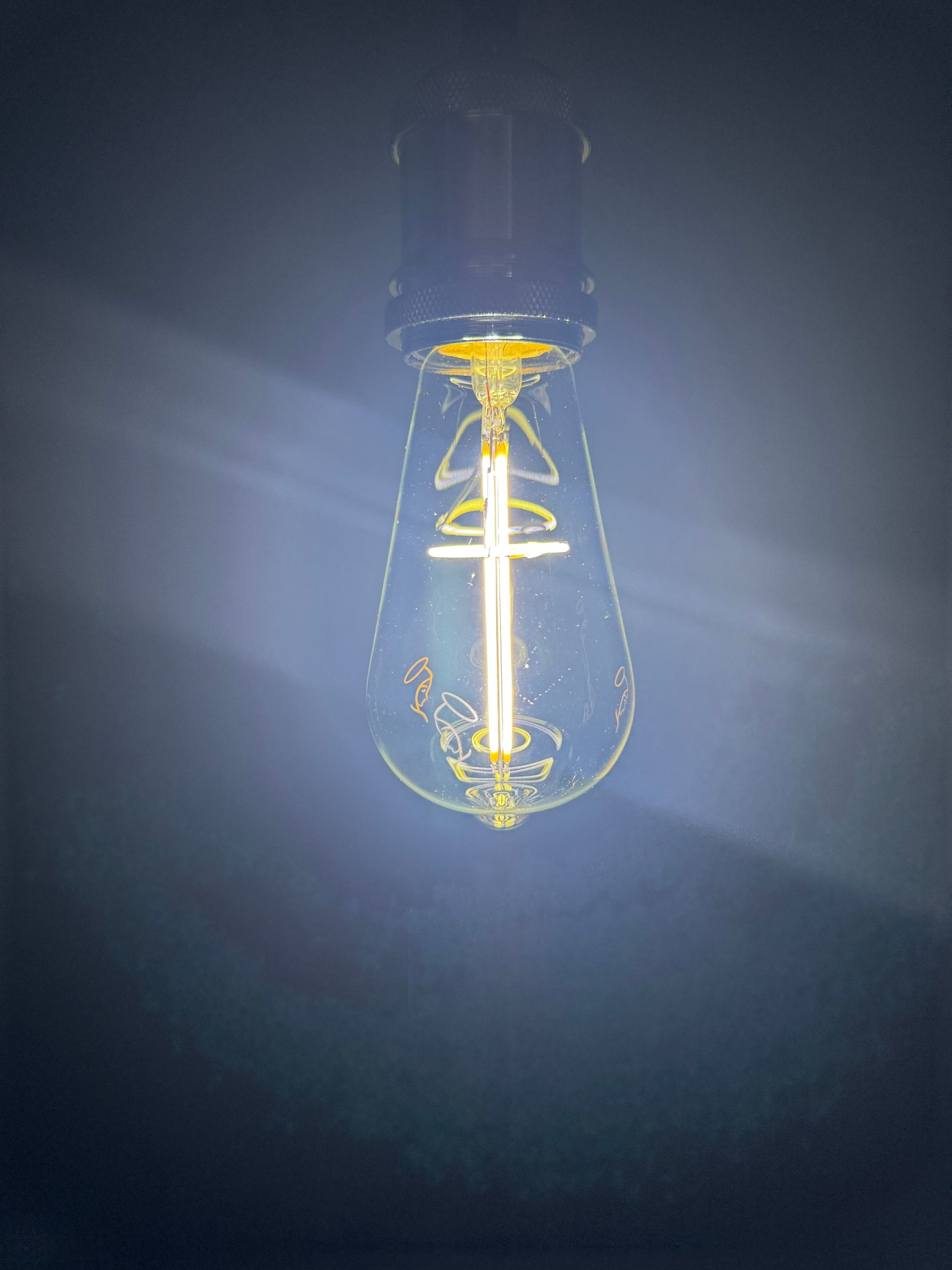 Lit, teardrop-shaped Edison lightbulb against a dark background, glowing with a bright, warm light.