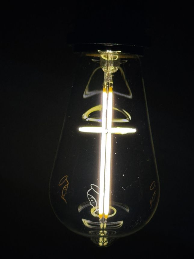 Lit, teardrop-shaped light bulb, glowing filament in dark setting.
