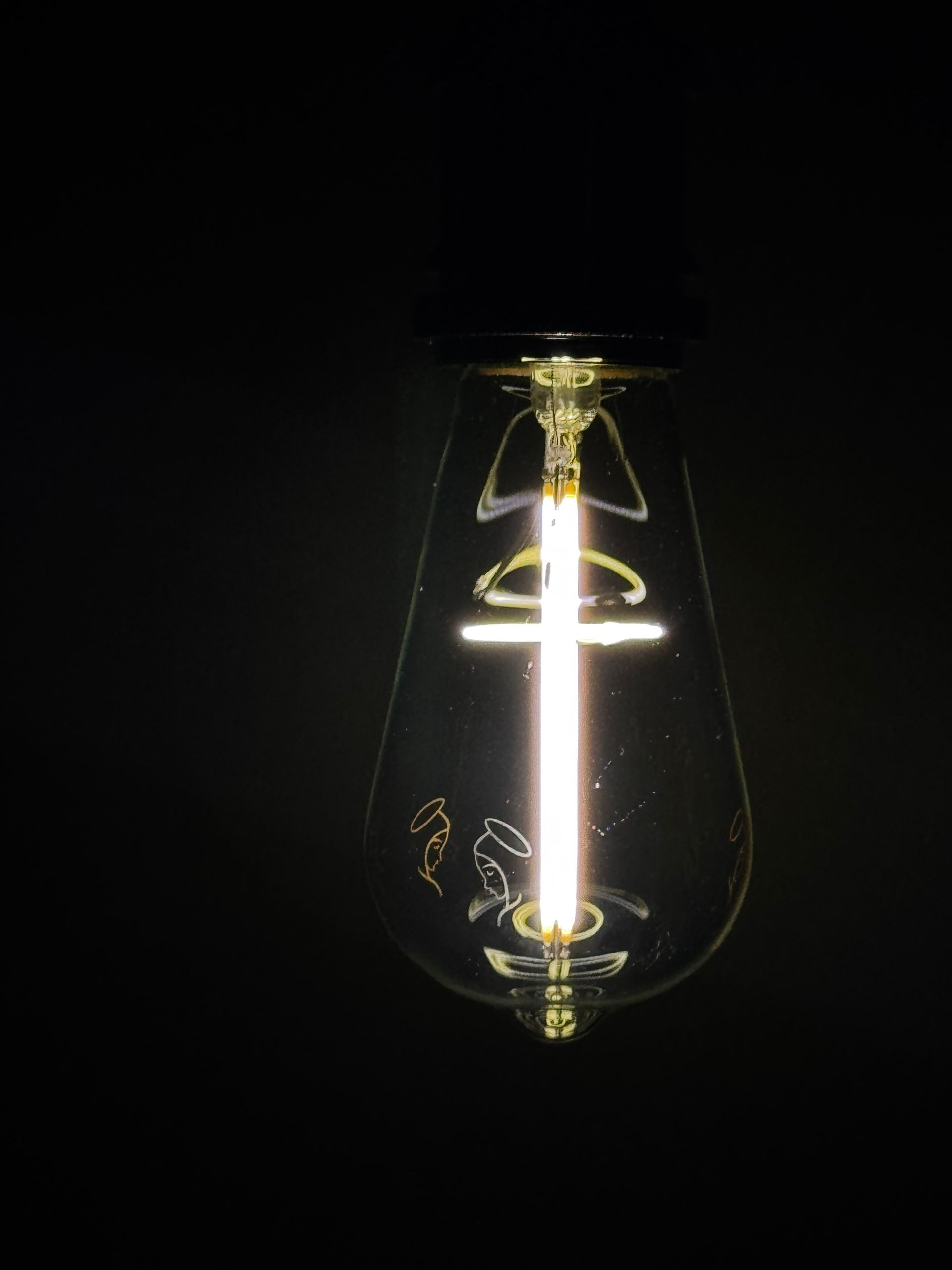 Lit LED light bulb in a dark room; vertical white light against a clear glass pear-shaped bulb.